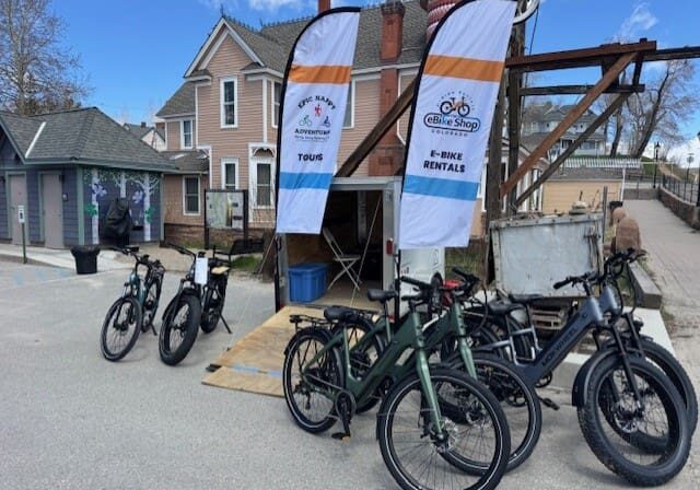 thumbnail_IMG_5577 E-bikes parked outside rental shop with banners.